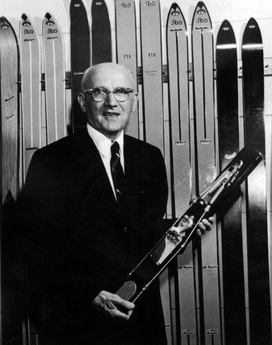 A man in a suit and tie is holding a pair of skis