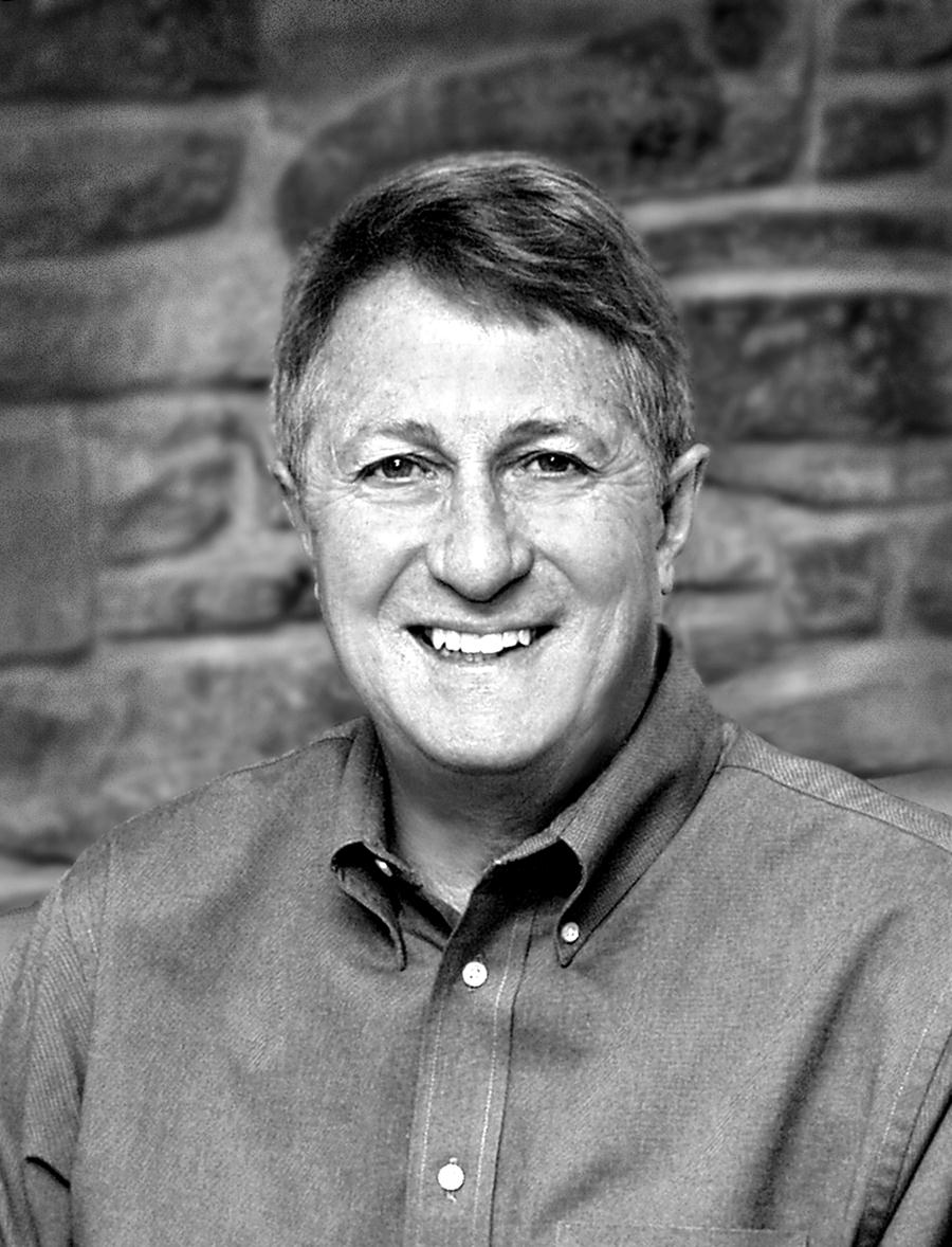 A man in a blue shirt is smiling in a black and white photo.