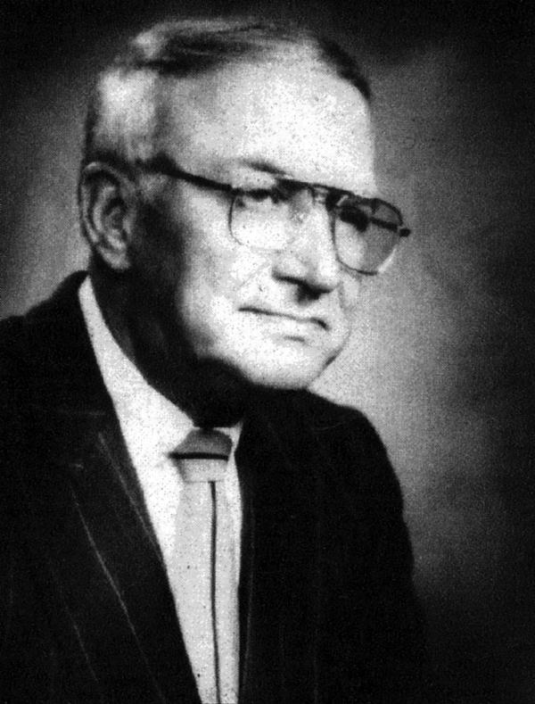 A black and white photo of a man wearing glasses and a suit and tie.