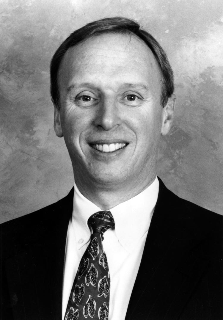 A man in a suit and tie is smiling in a black and white photo.