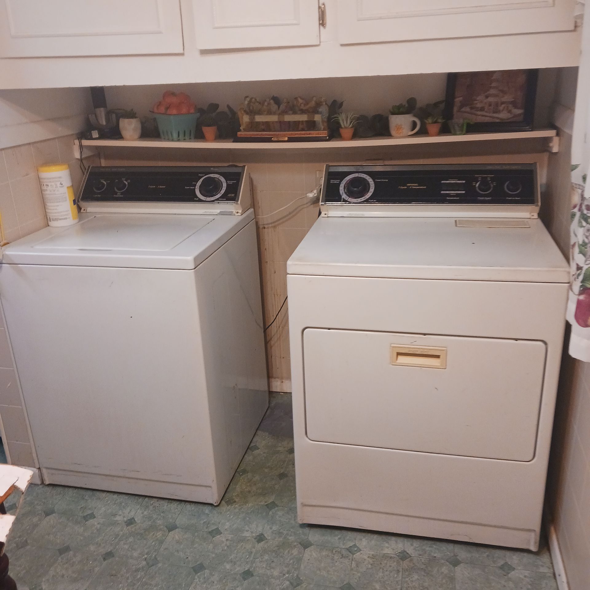 White washer and dryer set in a laundry room, with storage cabinets above.