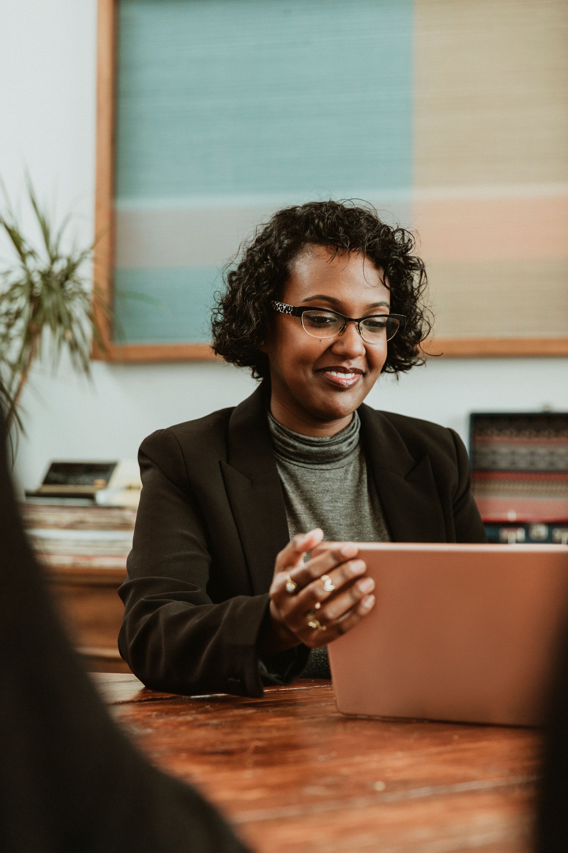 A woman is sitting at a table using a tablet computer to hire a career coach.