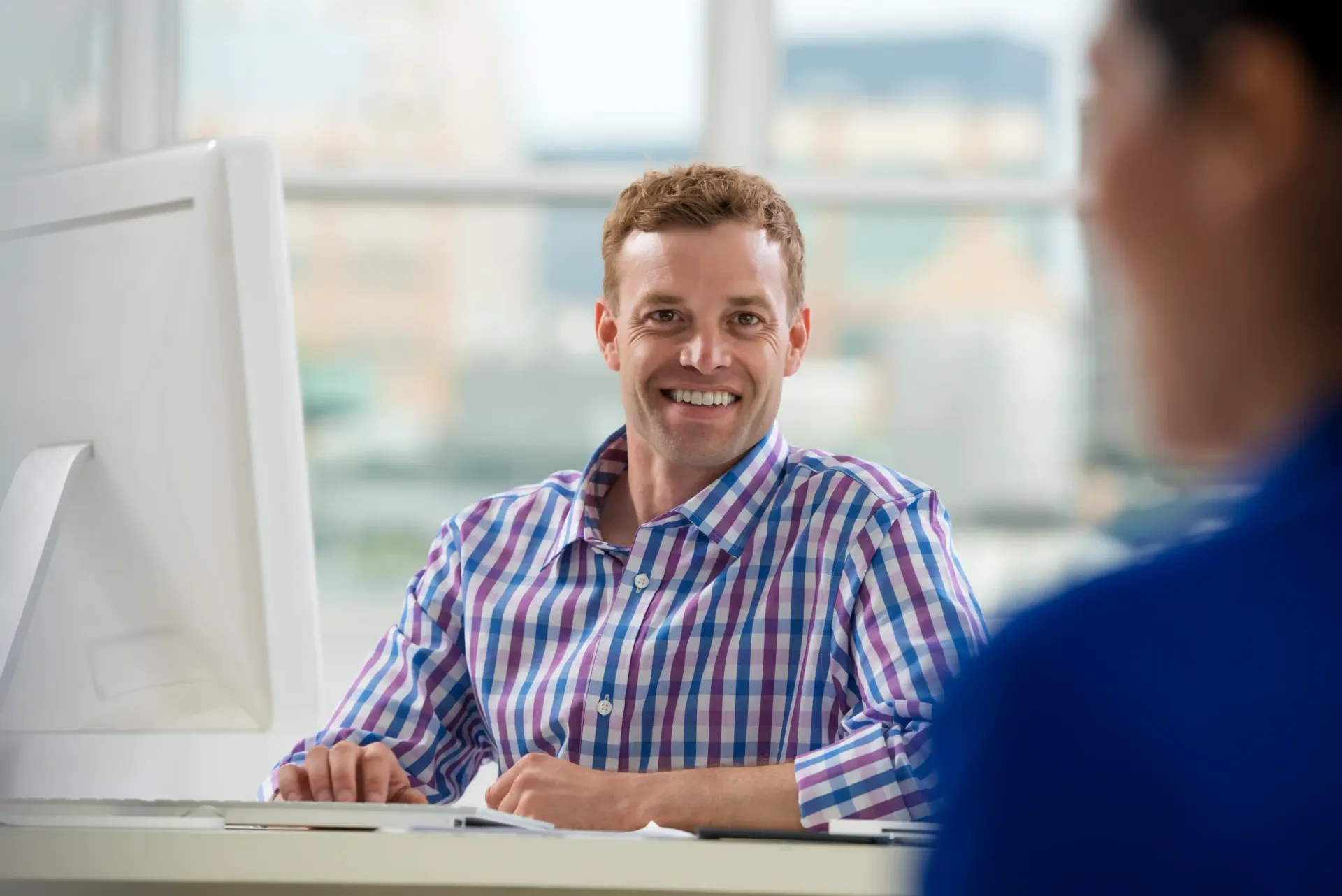 A man is smiling while sitting at a desk in front of a computer as he works on his personal branding.