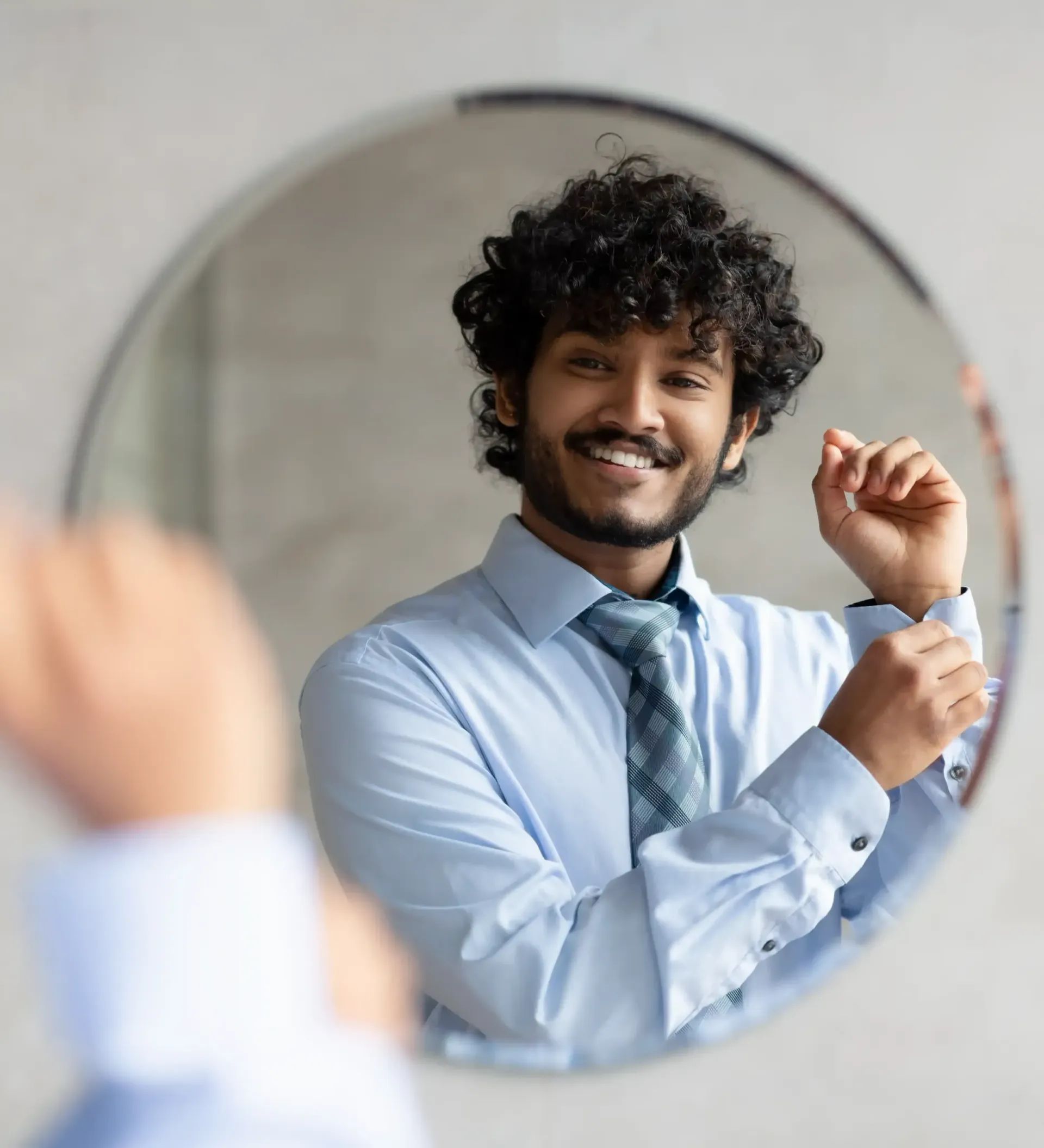 A man in a blue shirt and tie is adjusting his cufflinks in front of a mirror as he knows that a professional image is a strong part of personal branding.