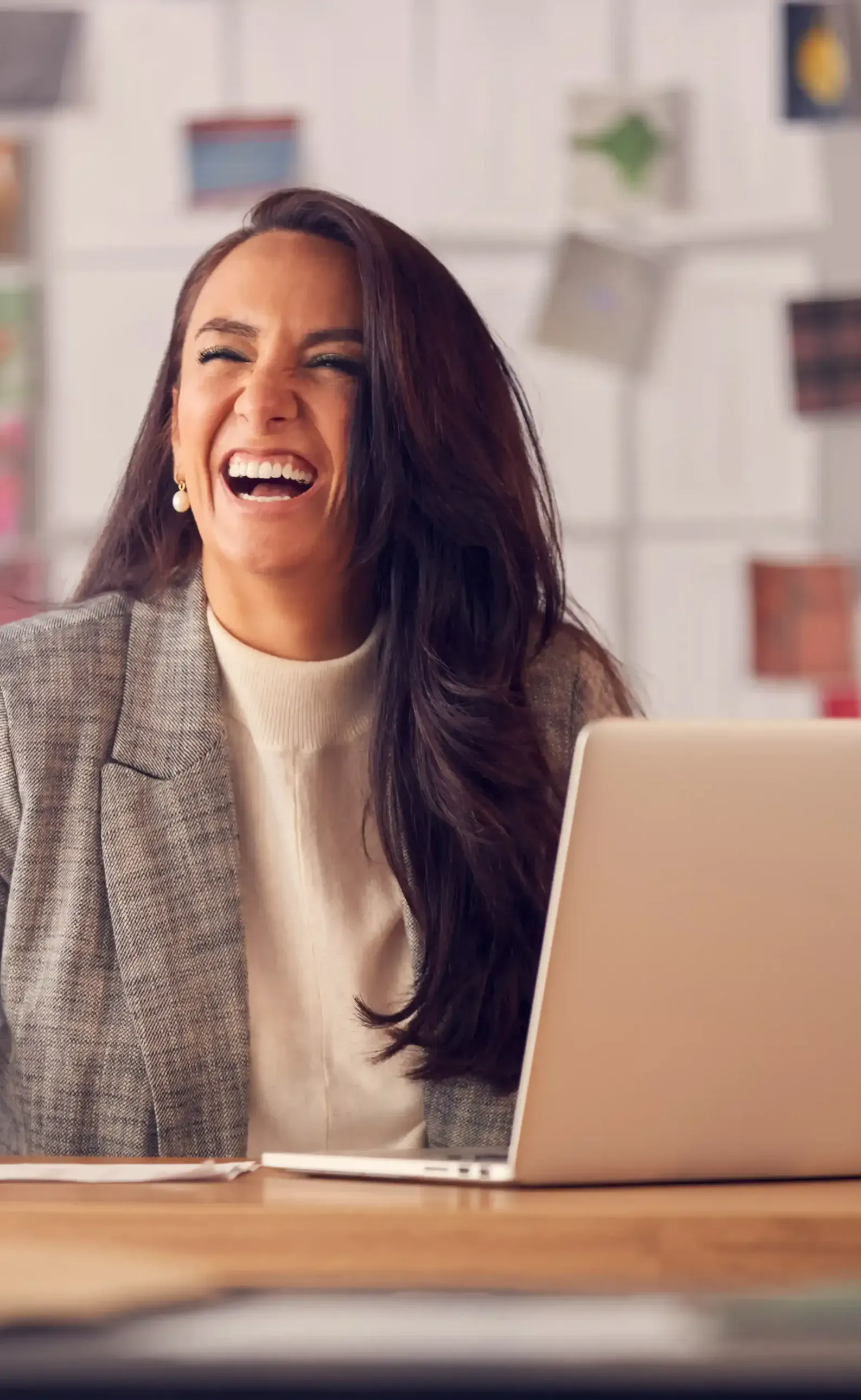 A woman is sitting at a desk with a laptop computer and laughing as she knows that constantly changing her personal brand to fit her growing self is beneficial.
