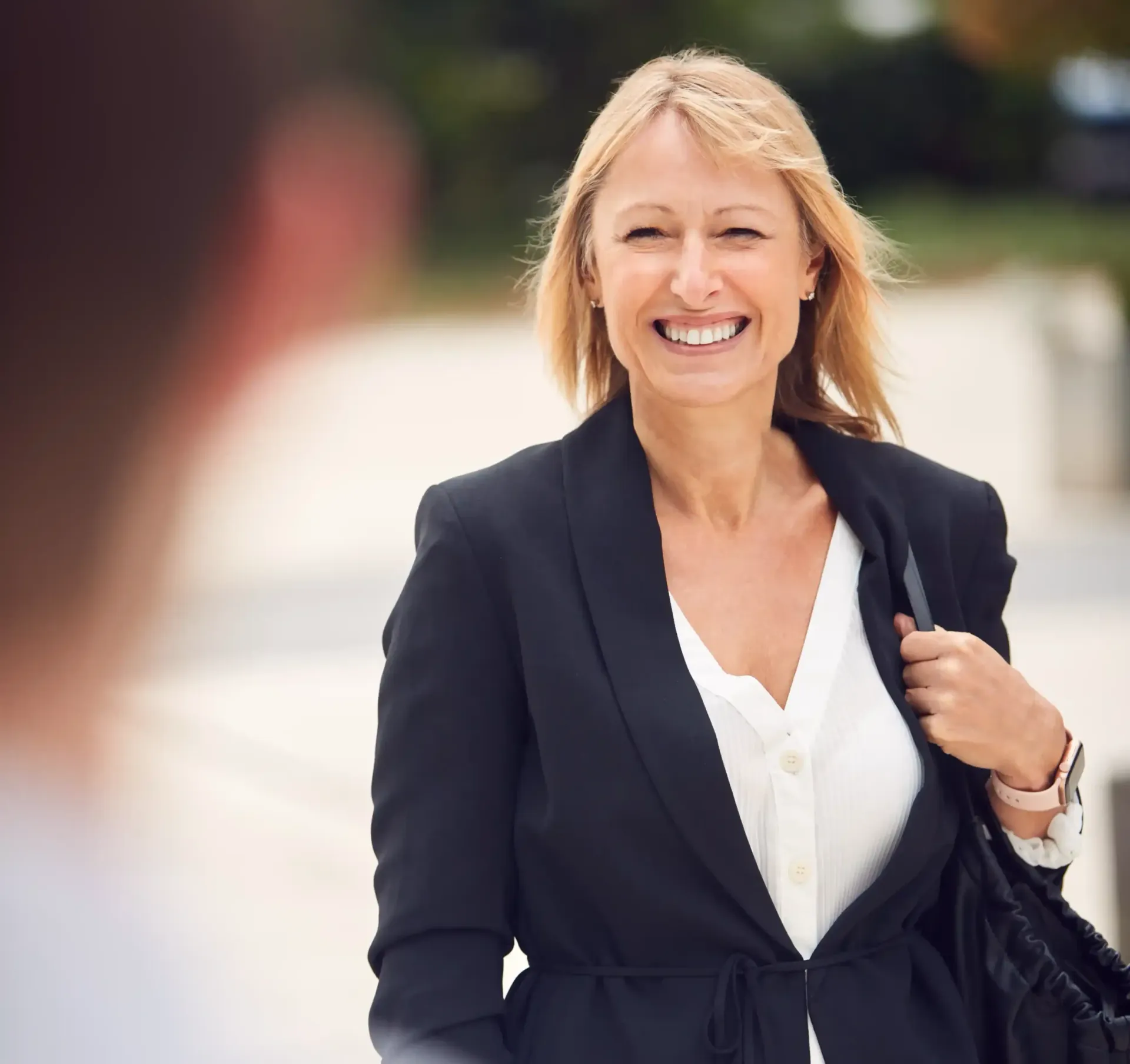 A woman in a black jacket and white shirt is smiling, approaching someone she met through her personal brand.
