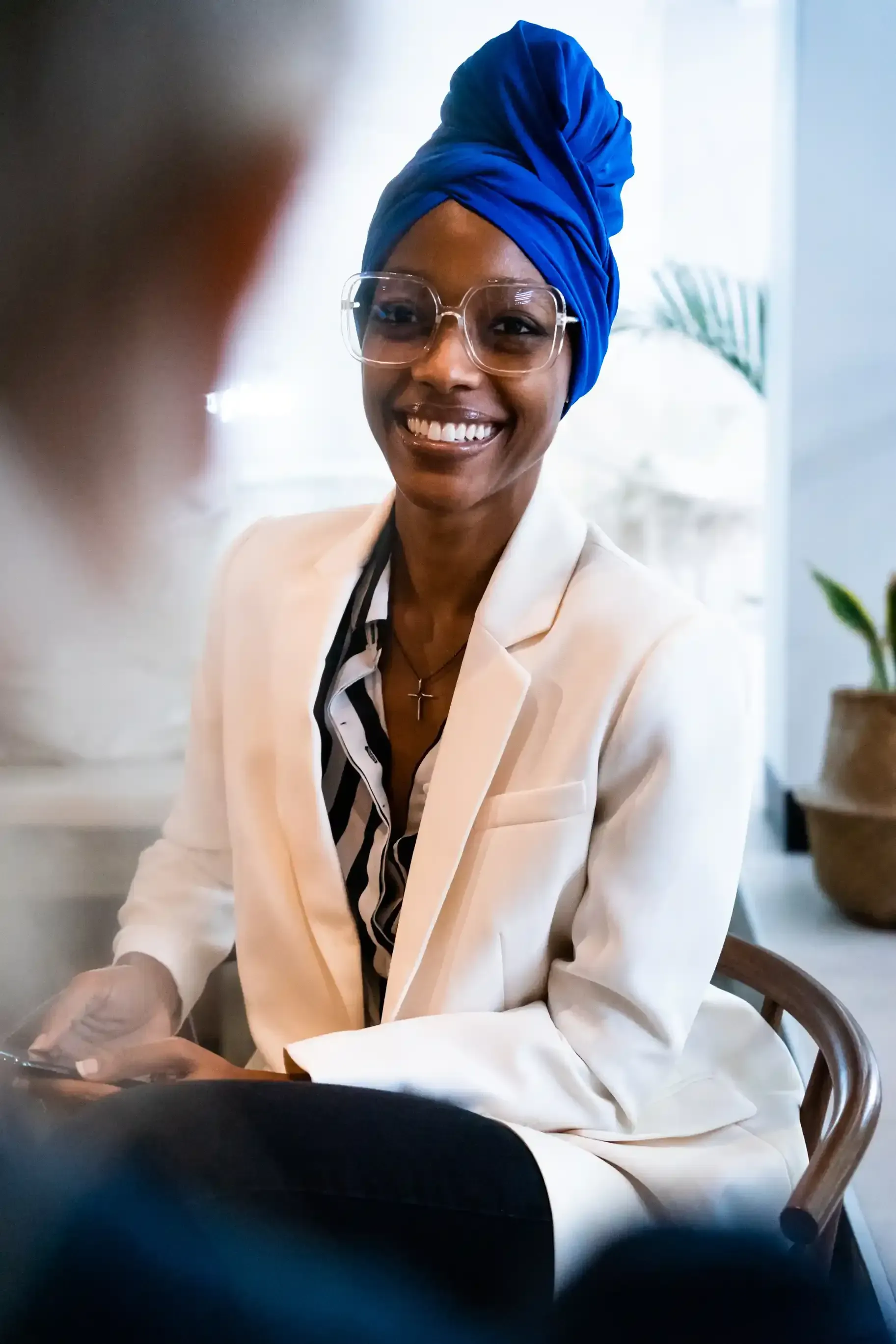 A woman wearing a blue turban and glasses is sitting in a chair and smiling as she discusses the benefits of personal branding with a career coach.
