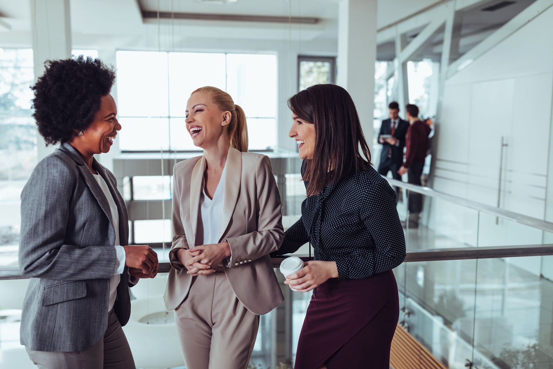 Three women are talking to each other in an office building at a networking event for senior level professionals.