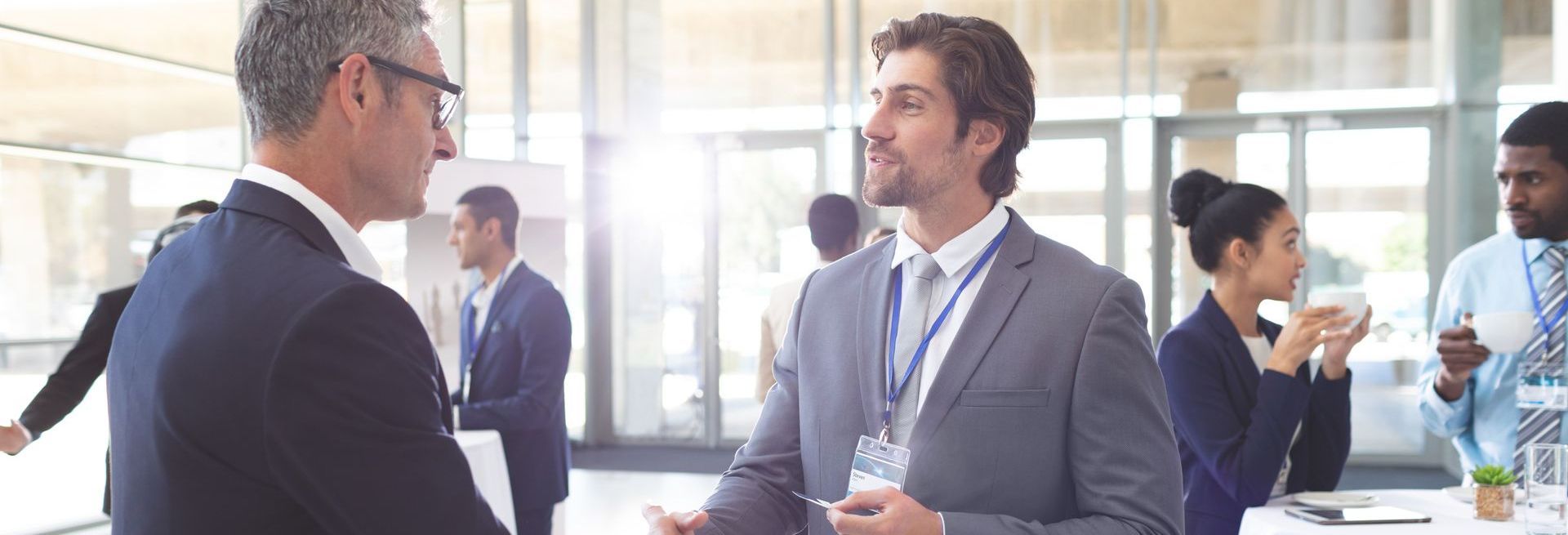 Two men are shaking hands at a networking event for senior level professionals.