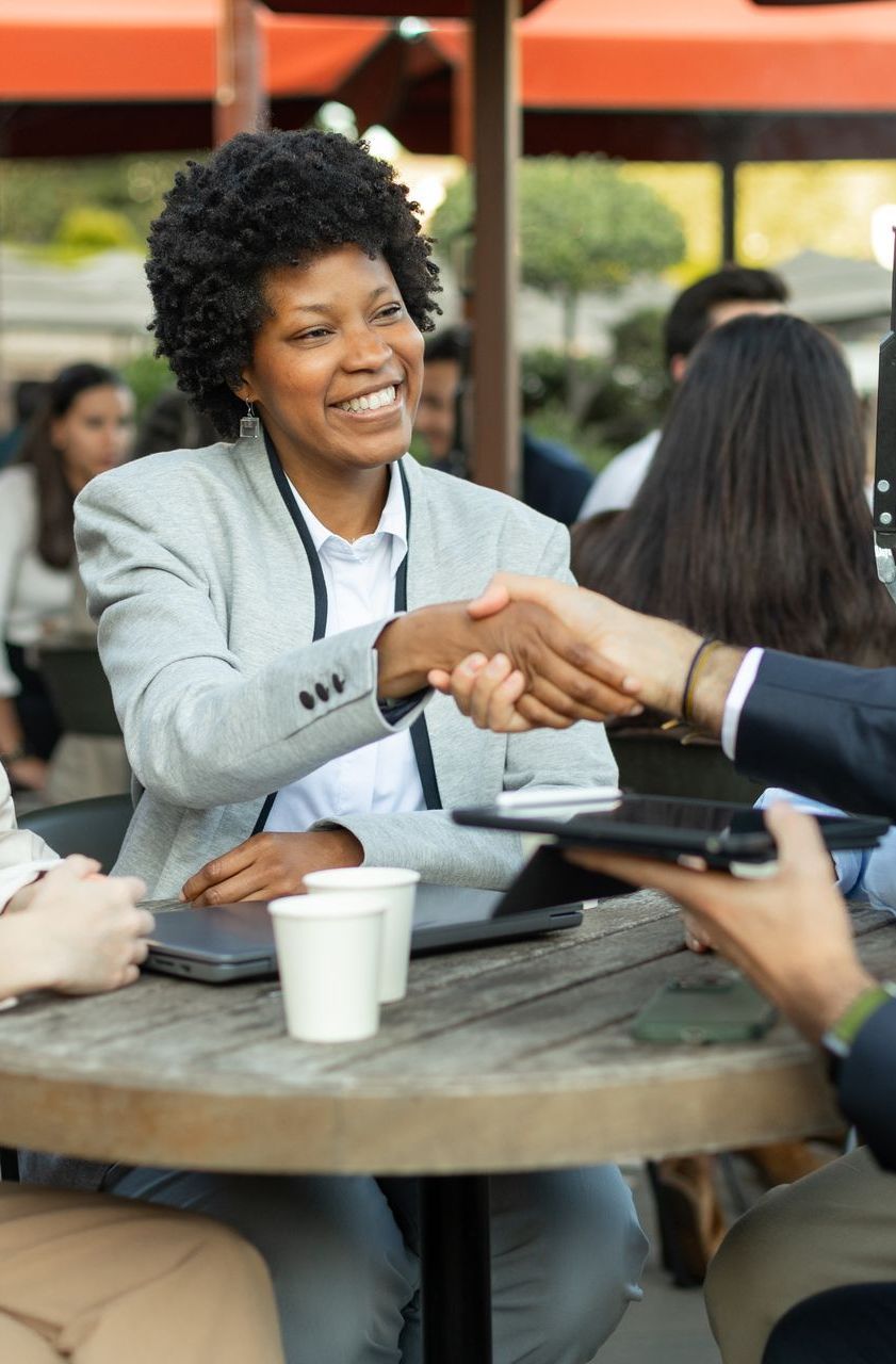 A woman is shaking hands with a man while sitting at a table and networking.