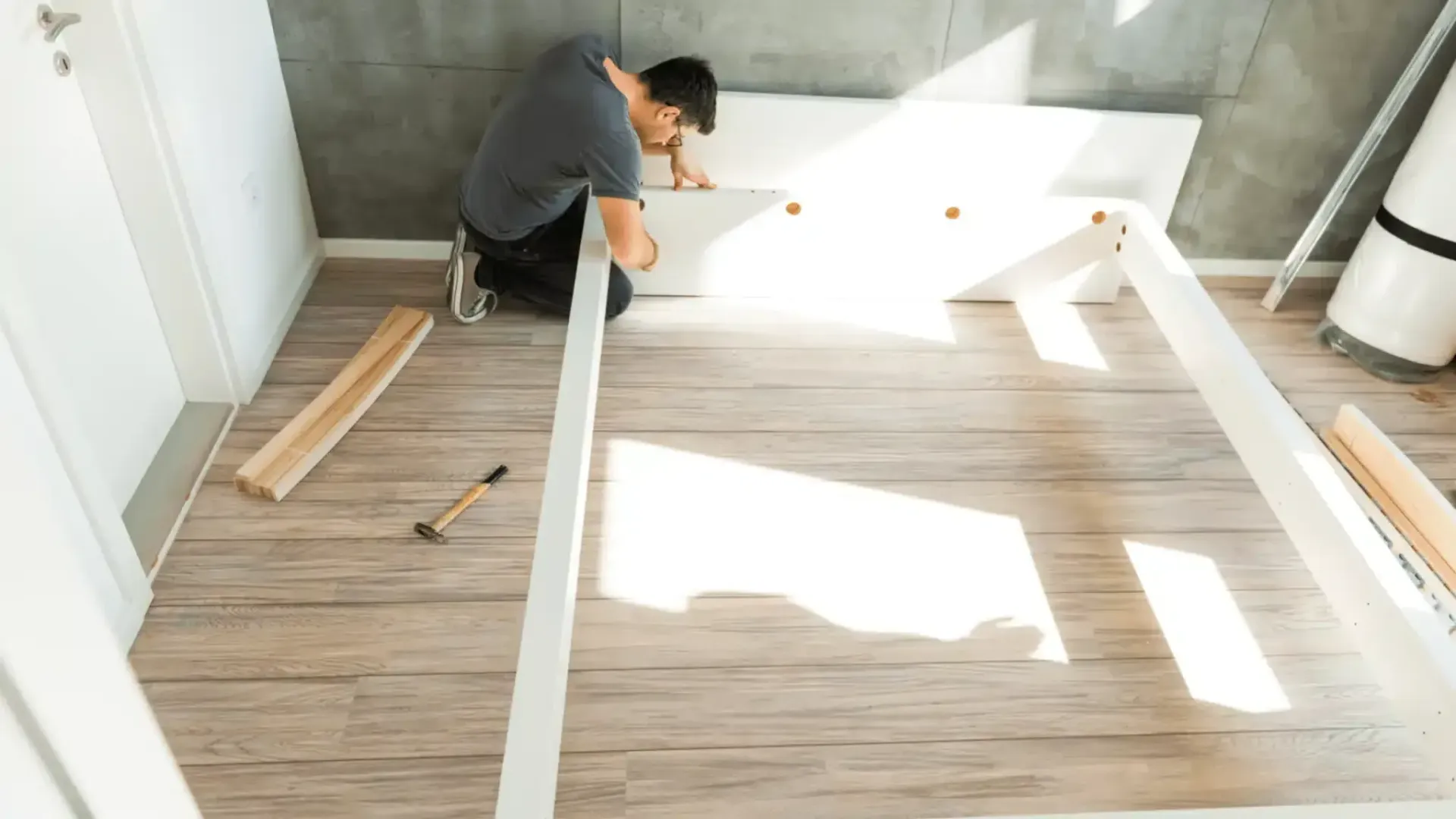 A Man is Kneeling Down and Working on a Bed Frame — Easy Choice Removals and General Freight In Port Macquarie, NSW
