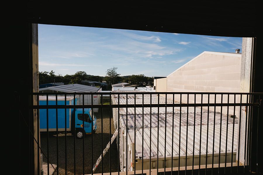 View Through a Railing: Blue Truck, Industrial Buildings, and a Blue Sky — Easy Choice Removals and General Freight In Maitland, NSW