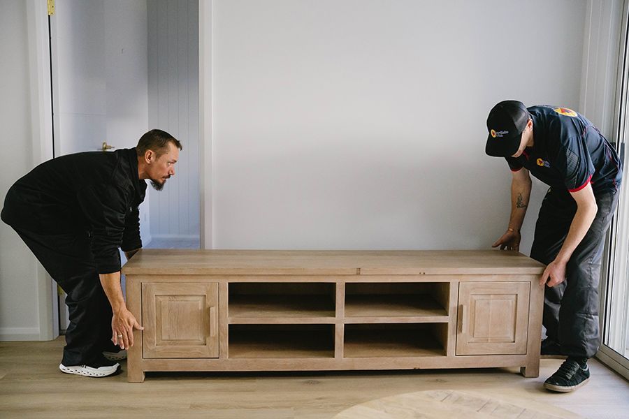 Two Movers Lifting A Wooden Tv Stand In An Empty Room — Easy Choice Removals and General Freight In Port Macquarie, NSW