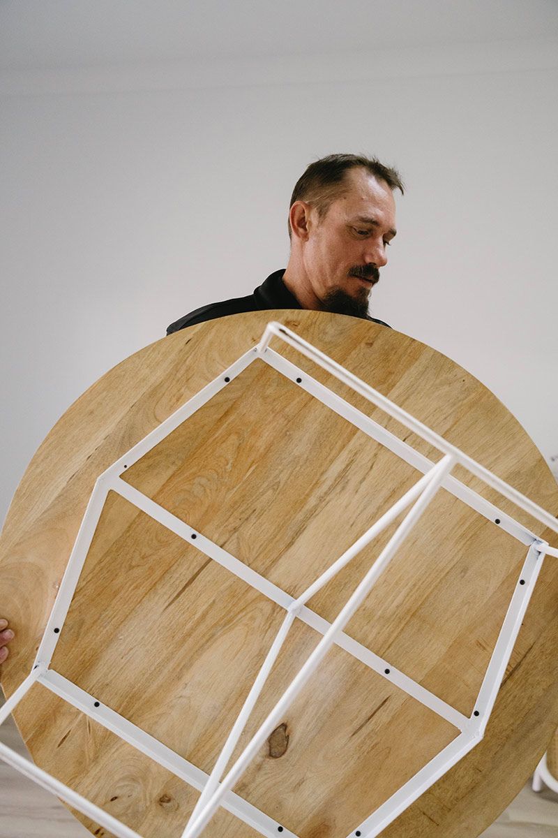 Man Holding up A Round Wooden Table — Easy Choice Removals and General Freight In Canberra, ACT