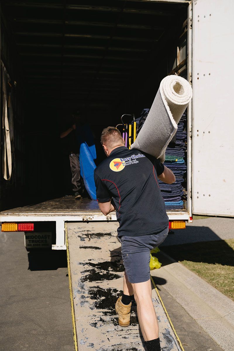 A Mover Carries a Rolled-up Rug Up a Ramp Into a Truck — Easy Choice Removals and General Freight In Port Macquarie, NSW
