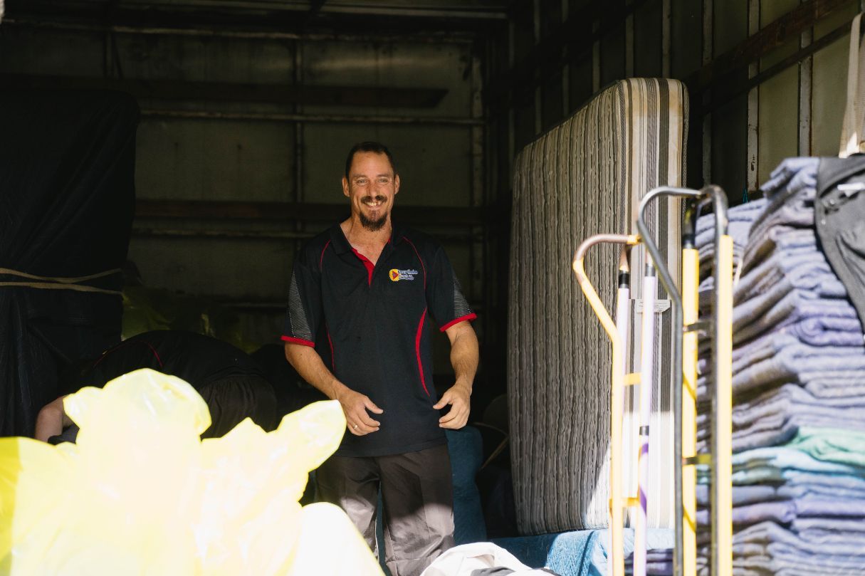 Man in Work Attire Smiles in a Storage Unit With Furniture — Easy Choice Removals and General Freight In Port Macquarie, NSW