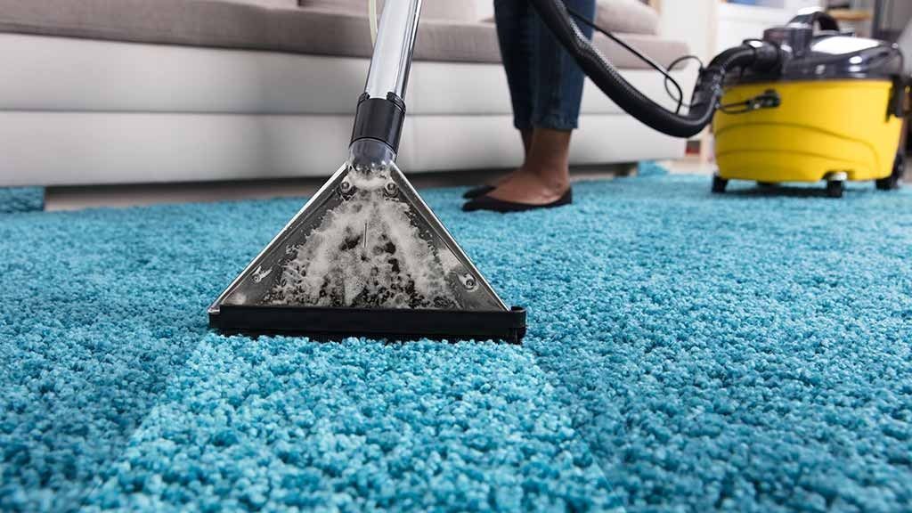 A Woman is Cleaning a Blue Carpet With a Vacuum Cleaner — Easy Choice Removals and General Freight In Port Macquarie, NSW