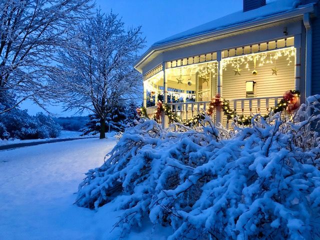 A house with a porch decorated for christmas is covered in snow