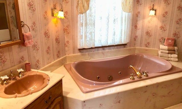 A bathroom with a pink tub , sink and mirror.