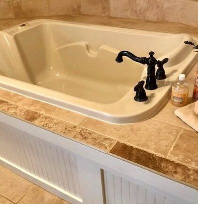 A white bathtub with black faucets is sitting on a tiled counter top.