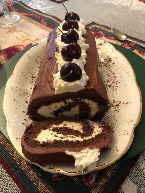 A chocolate cake roll with whipped cream and cherries on top