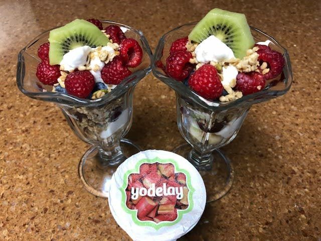 Two glasses of yogurt with raspberries and kiwi next to a jar of yodelay