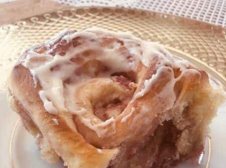 A cinnamon roll with icing on a white plate.