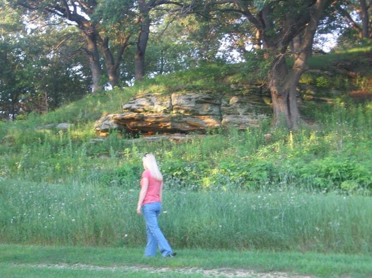 A woman in a red shirt is walking through a grassy field