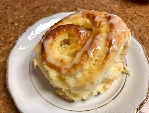 A cinnamon roll with icing on a white plate.