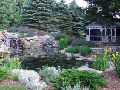 There is a gazebo in the middle of a pond with a waterfall in the background.