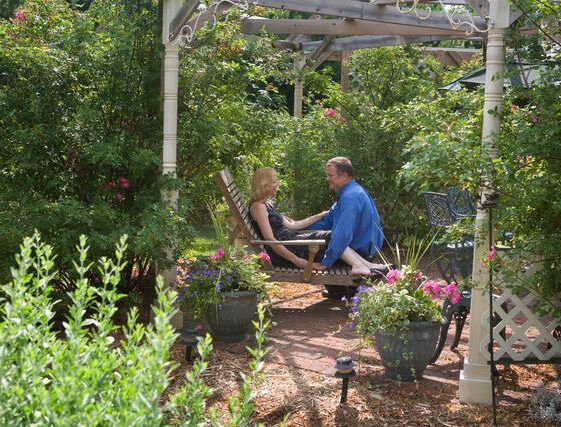 A man and a woman are sitting under a pergola in a garden.