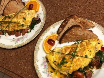 Two plates of omelet with toast and oranges on a table.