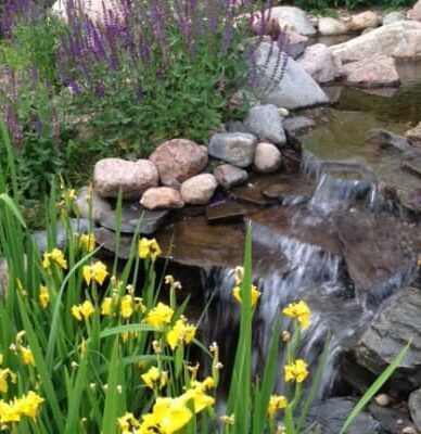 A waterfall surrounded by flowers and rocks in a garden.