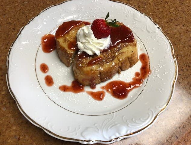 A white plate topped with a piece of french toast with whipped cream and a strawberry on top.