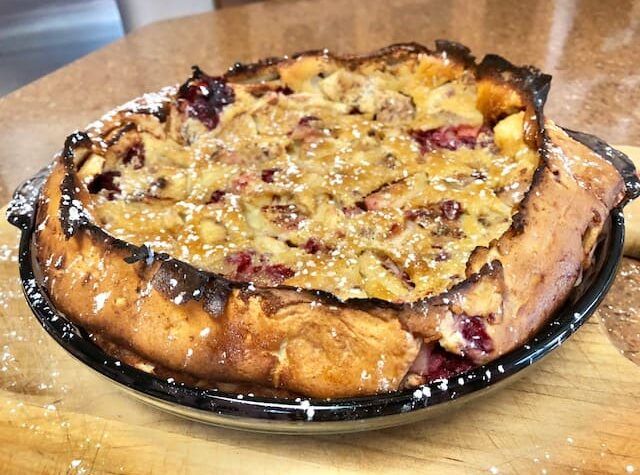 A pie with powdered sugar on top is on a wooden table.