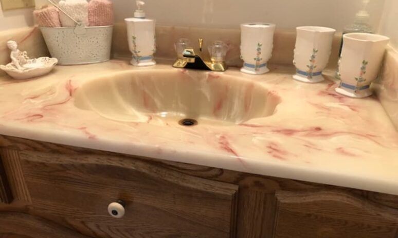 A bathroom sink with a pink counter top and a wooden cabinet.