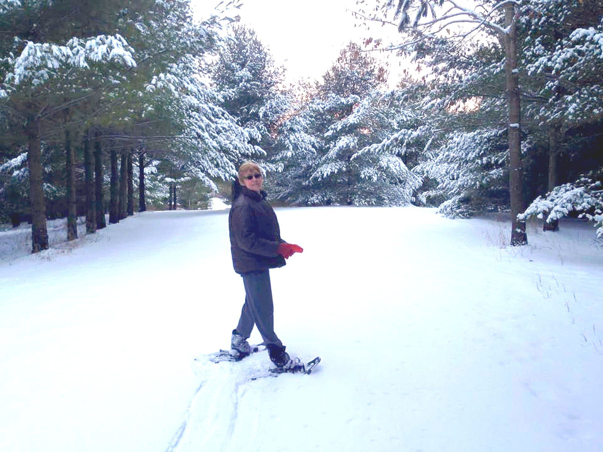 A woman is walking down a snowy road wearing snow shoes