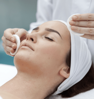 A woman is getting her face cleaned with cotton pads