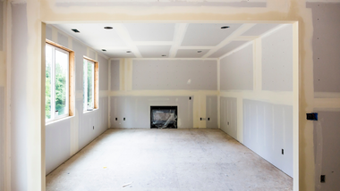 Empty unfinished room with white walls, windows, and a small fireplace alcove.