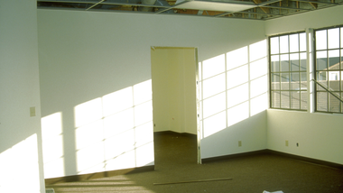Empty sunlit room with white walls, large windows, and an open doorway