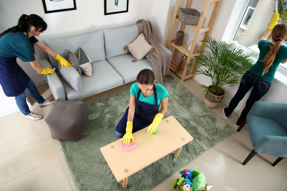 Two Women Are Cleaning A Living Room With A Couch And A Table — Super Home Cleaning Services In Manunda, QLD 