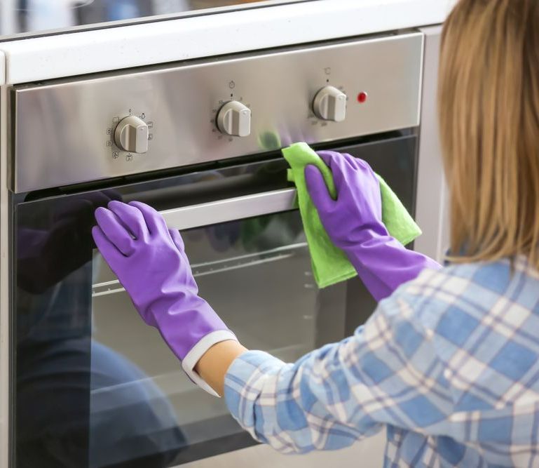 A Woman Wearing Purple Gloves Is Cleaning An Oven With A Cloth — Super Home Cleaning Services In Manunda, QLD