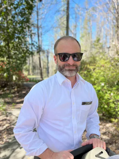 Blue wooden door with silver handle and shutter against white siding.