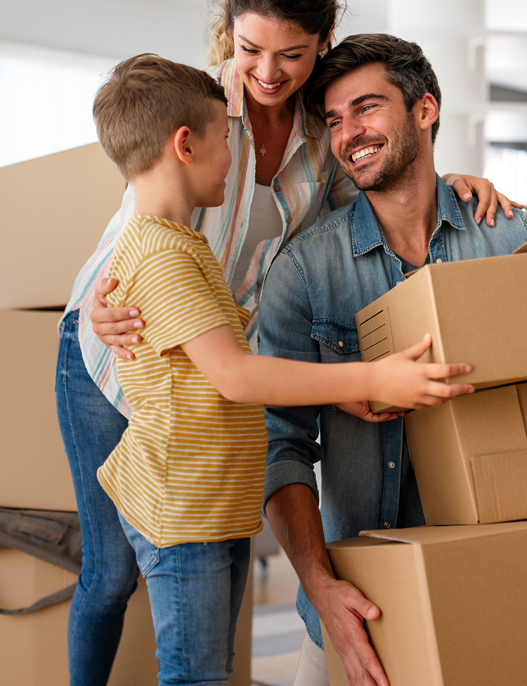 Family of three smiles while moving boxes, embracing; woman has arm around son.