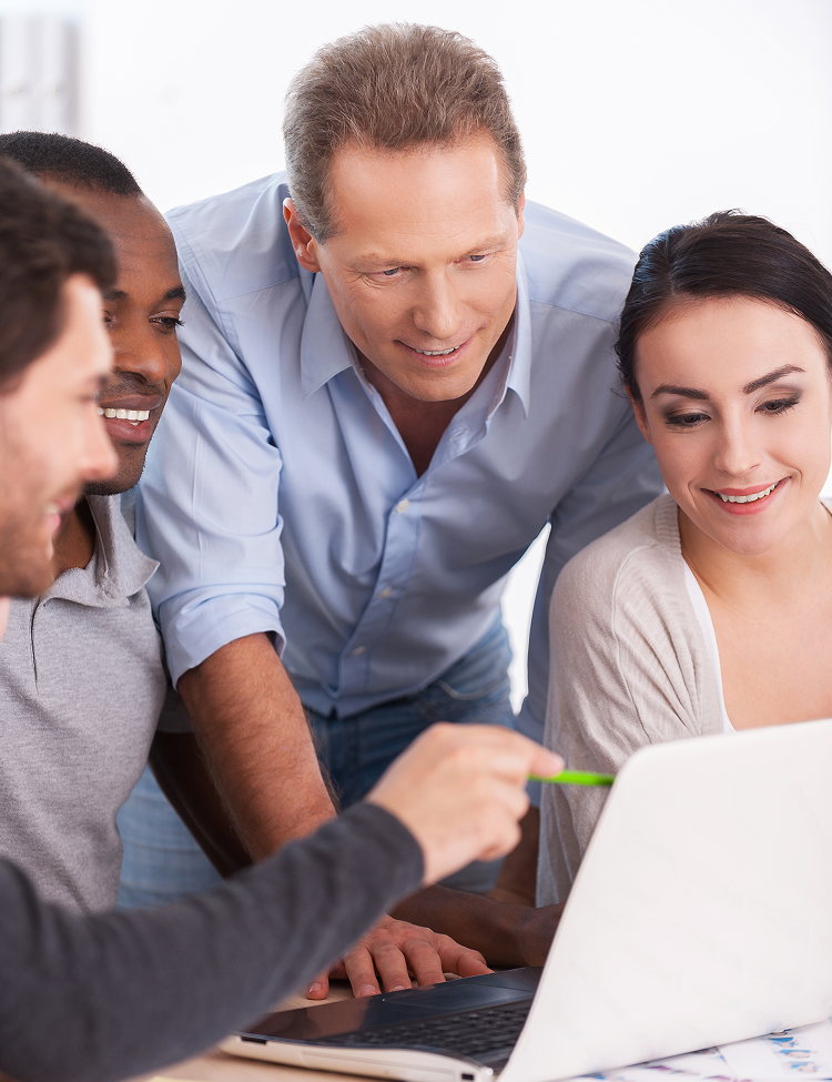Team of five colleagues collaborating around a laptop, pointing and smiling, indoors.