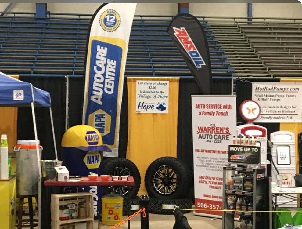 Auto parts display with racing signs, tires, tools, and car-care banners in a garage-like booth | CB Warren's Auto Care