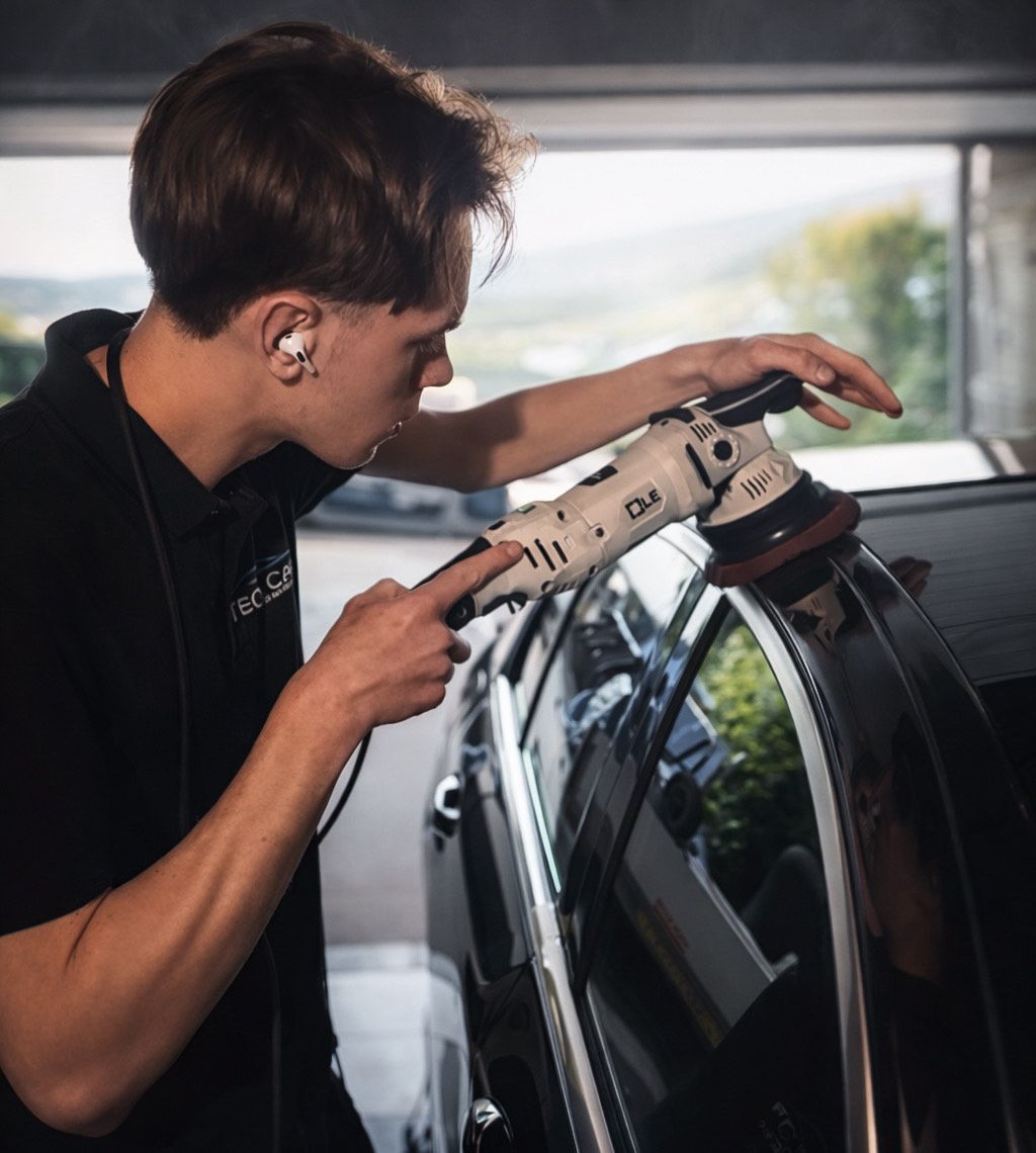 Een persoon die buiten een zwarte auto oppoetst en polijst met een witte polijstmachine, bij een zwarte auto.