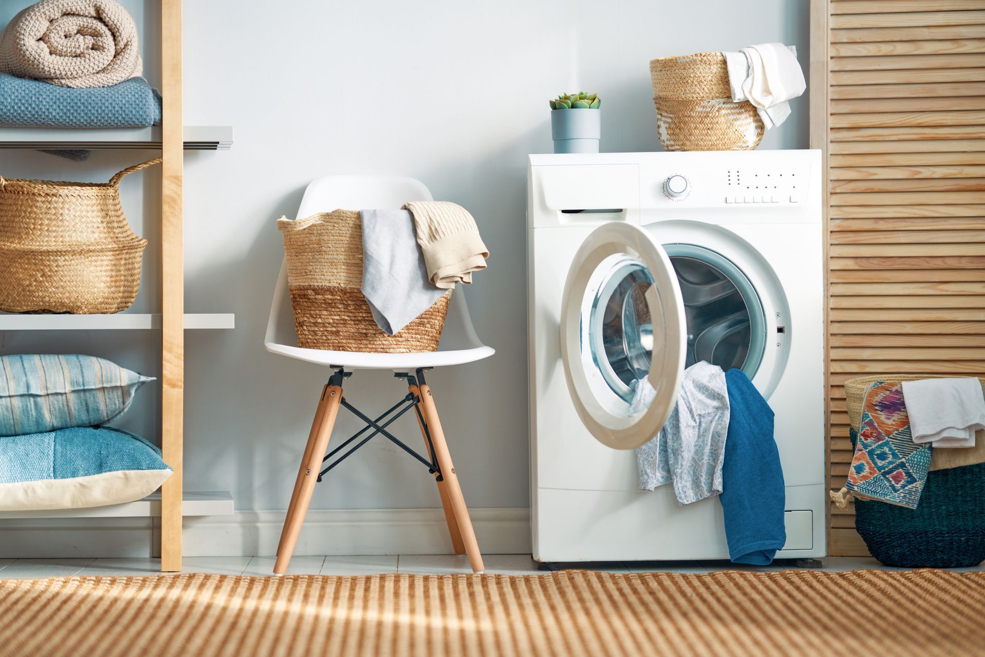 Laundry room with washing machine, laundry baskets, and a chair holding a basket of clothes.
