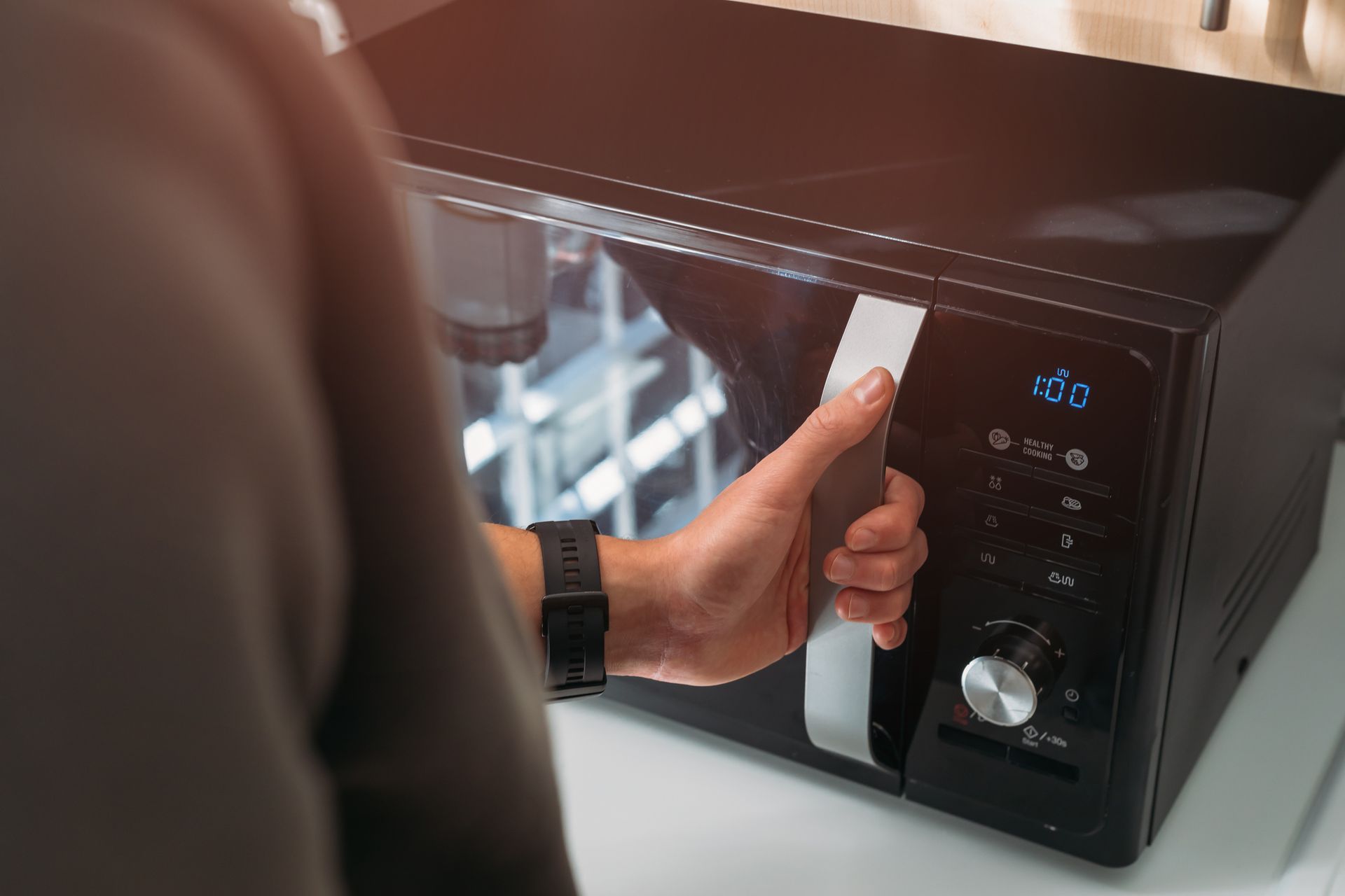 Person opening a black microwave door. The setting appears to be a kitchen.