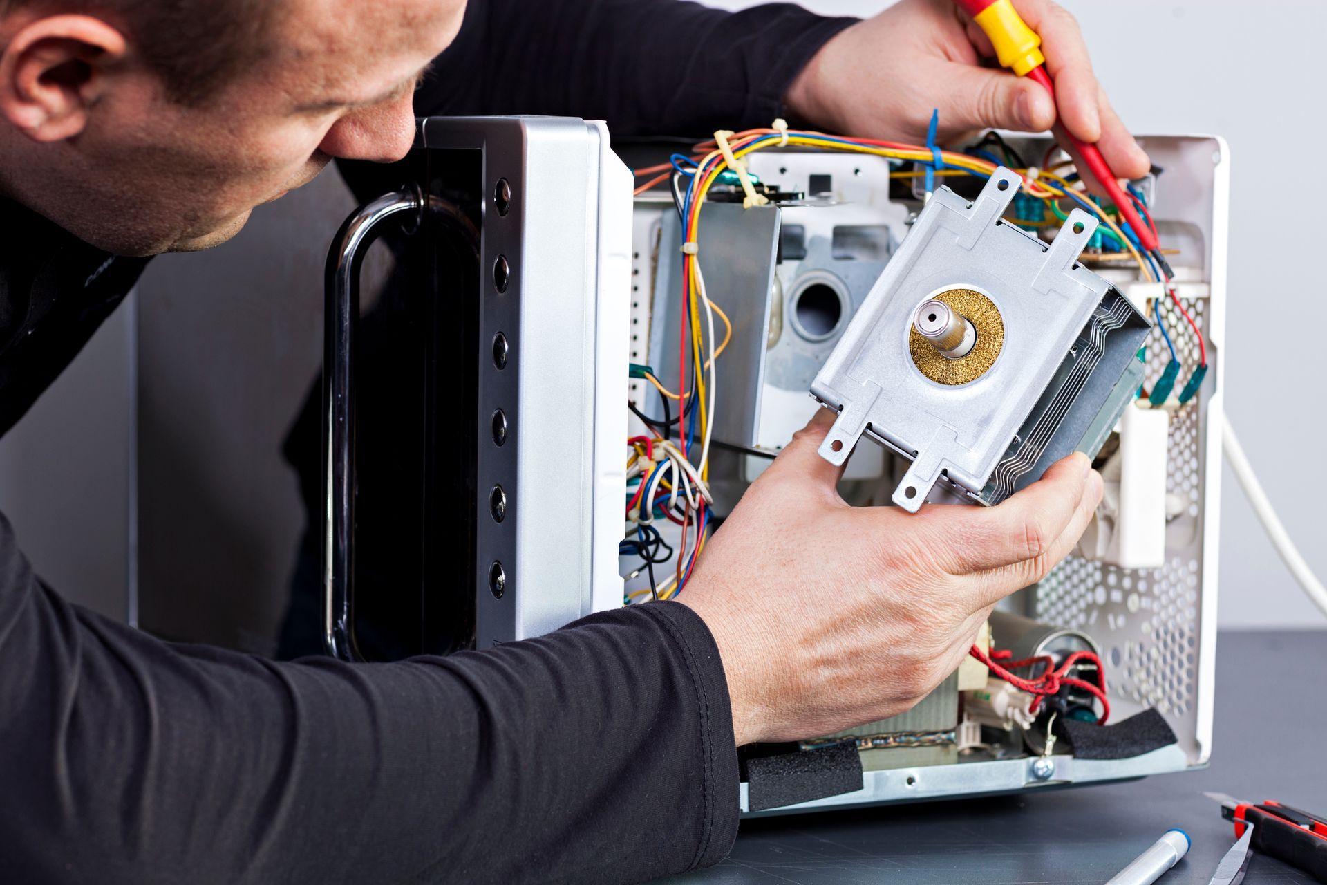 Man repairing a microwave, using screwdriver. Wires and components visible.